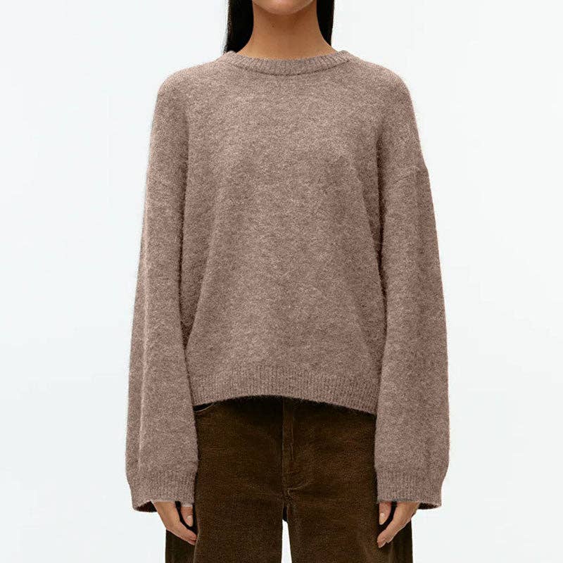 A person wearing an oversized, long-sleeve knit sweater in a heathered taupe-brown color, paired with dark brown corduroy pants, against a plain white background.