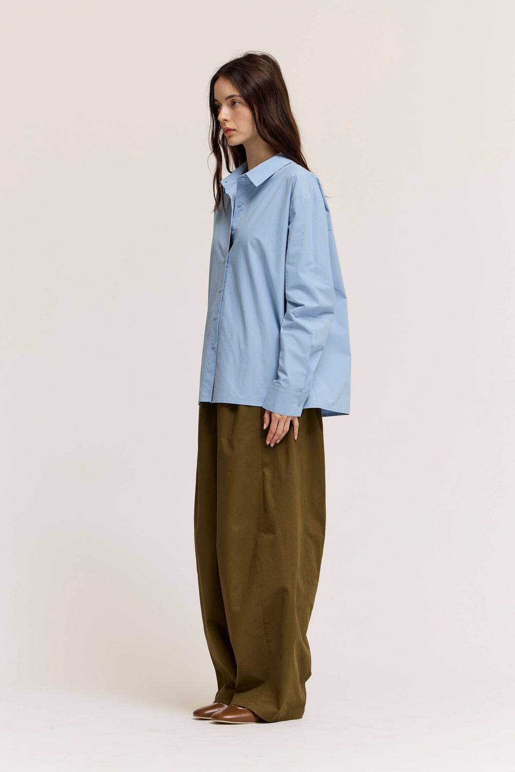 Person wearing a light blue shirt and olive green pants on a white background