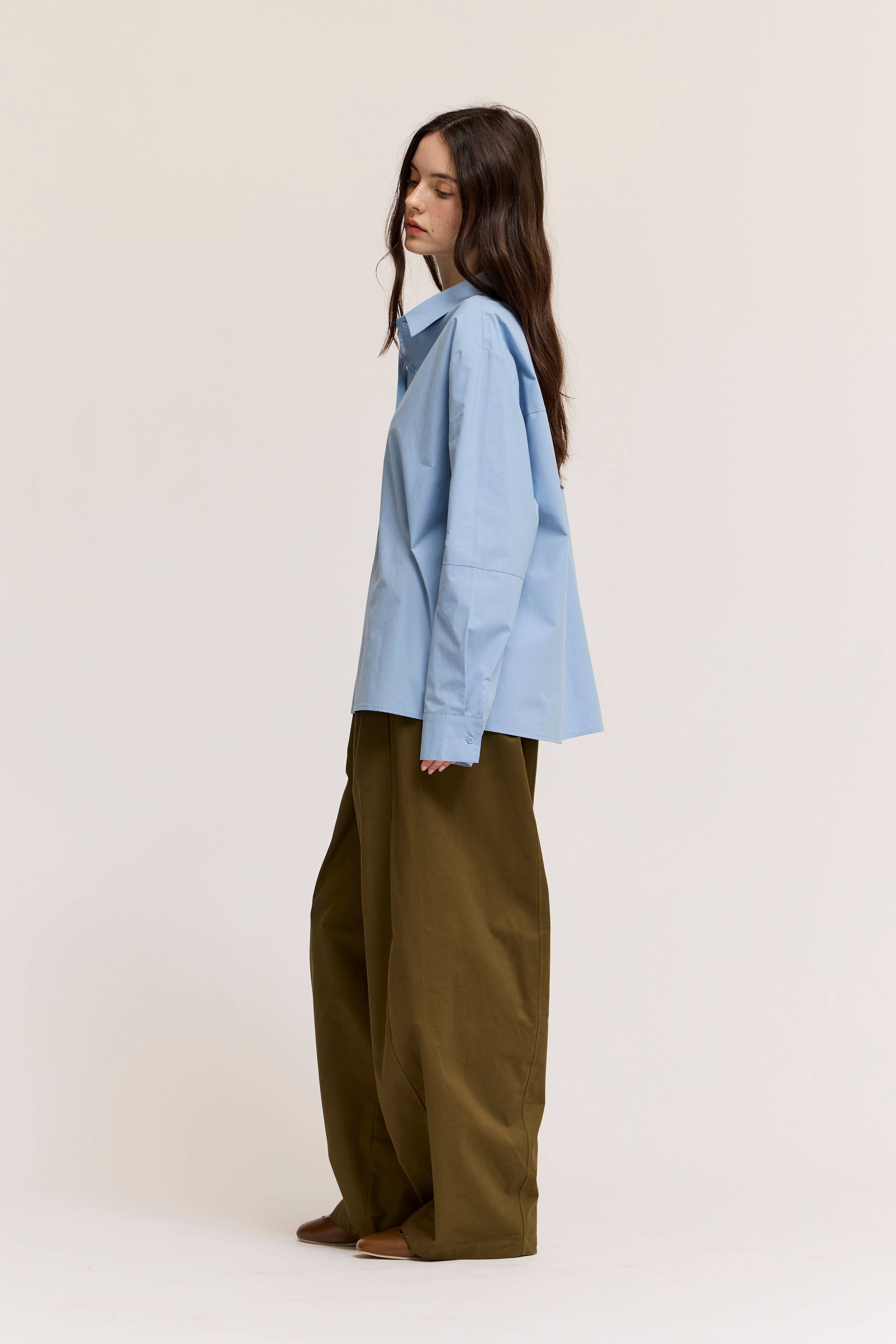 Woman wearing a light blue shirt and olive green pants on a white background