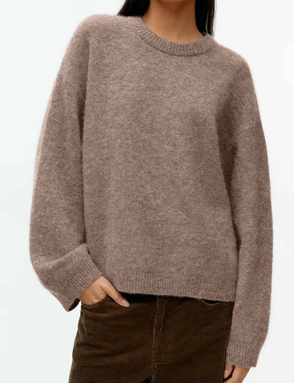 A person wearing a soft, oversized crewneck sweater in a heathered taupe-brown color, paired with dark brown corduroy pants, against a plain white background.
