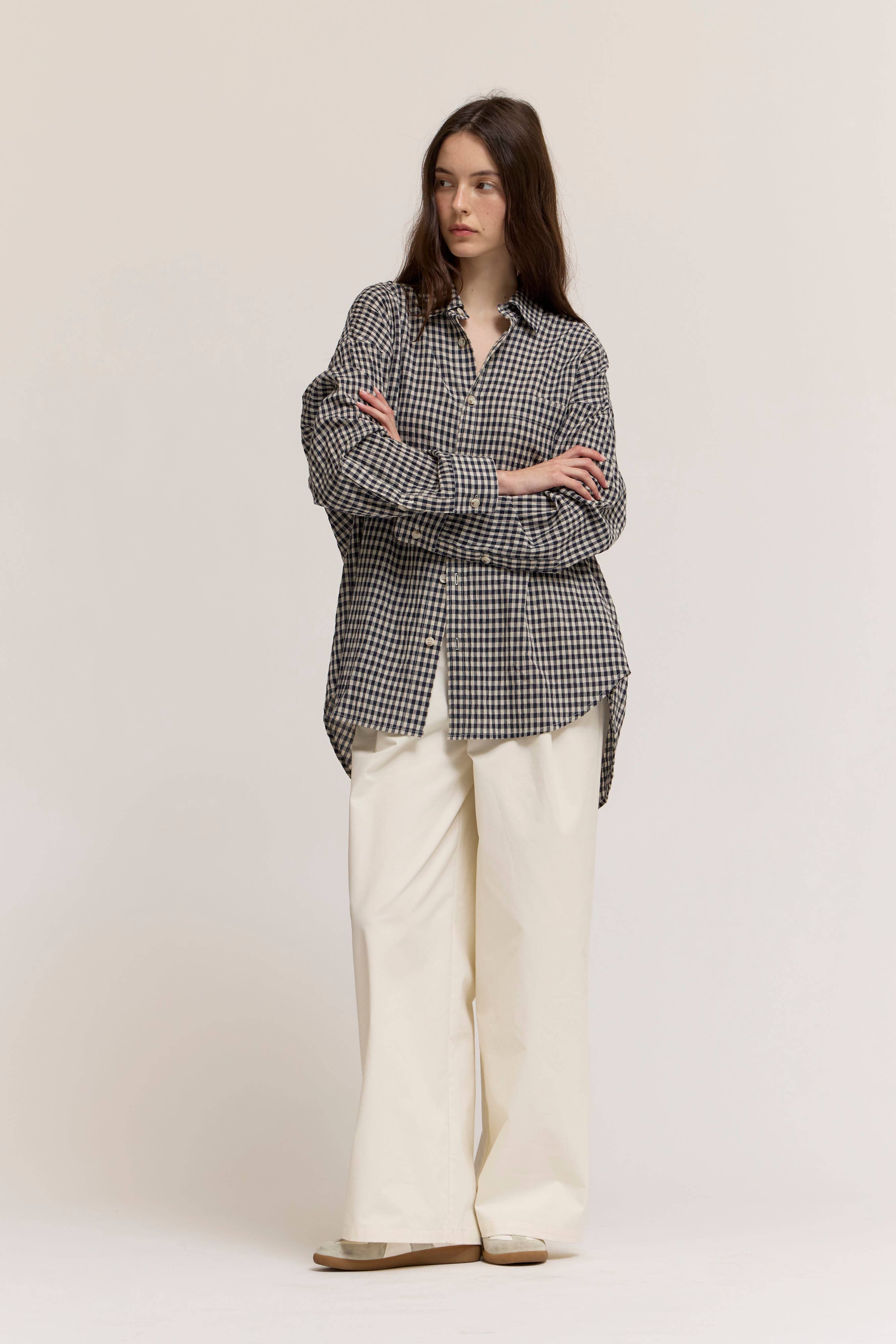 Woman wearing a checkered shirt and white pants on a plain background