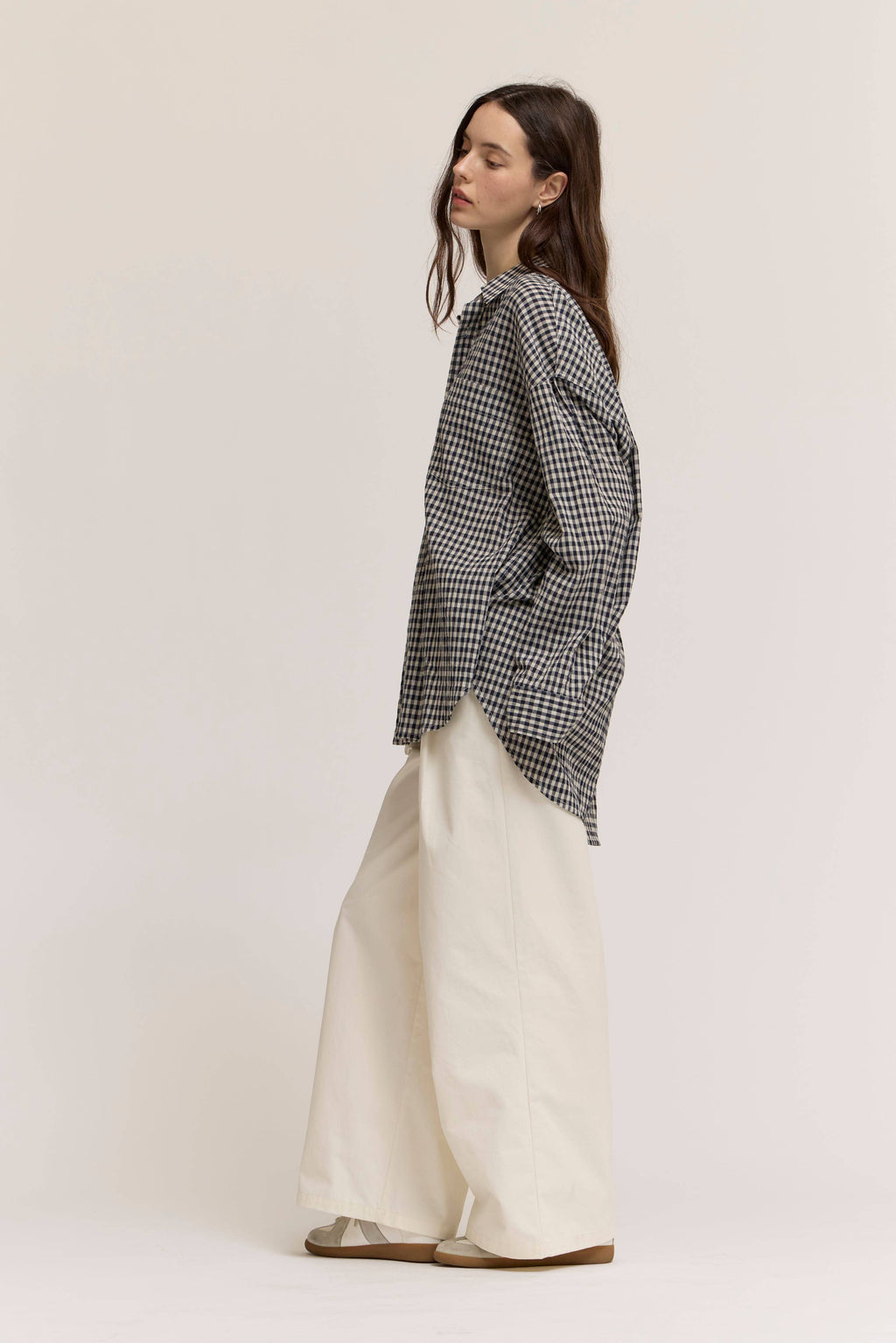 Woman wearing a black and white checkered shirt and white pants on a plain background