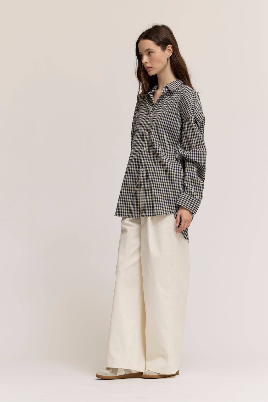 Woman wearing a black and white checkered shirt and white pants on a plain background