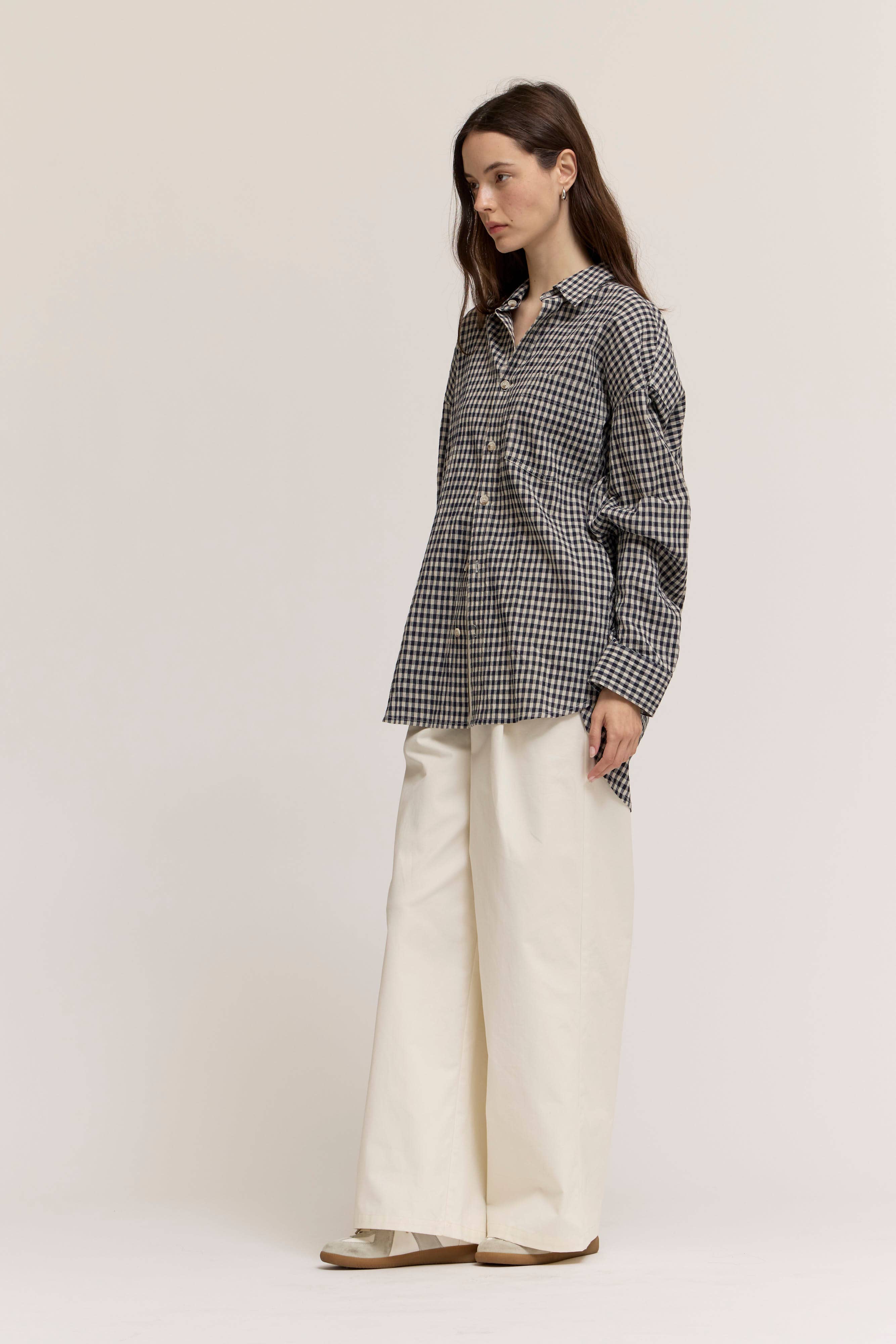 Woman wearing a black and white checkered shirt and white pants on a plain background