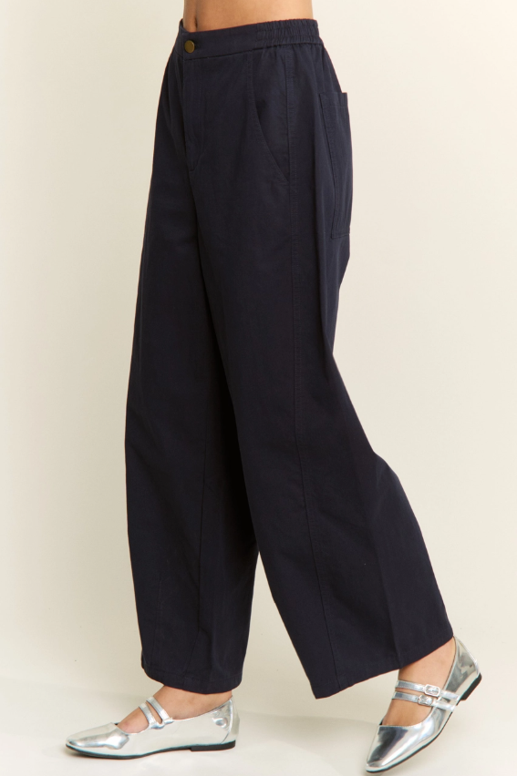 A person wearing dark navy wide-leg cropped pants with side pockets and metallic silver flat shoes, shown against a plain light beige studio background.