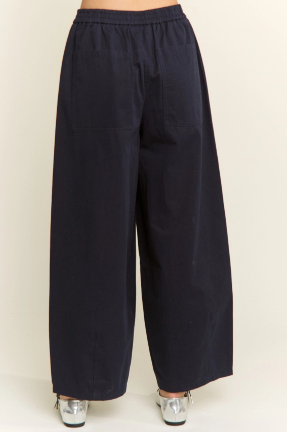 A person wearing loose, wide-leg cropped pants in a very dark navy color, shown from the waist down against a plain light beige studio background.