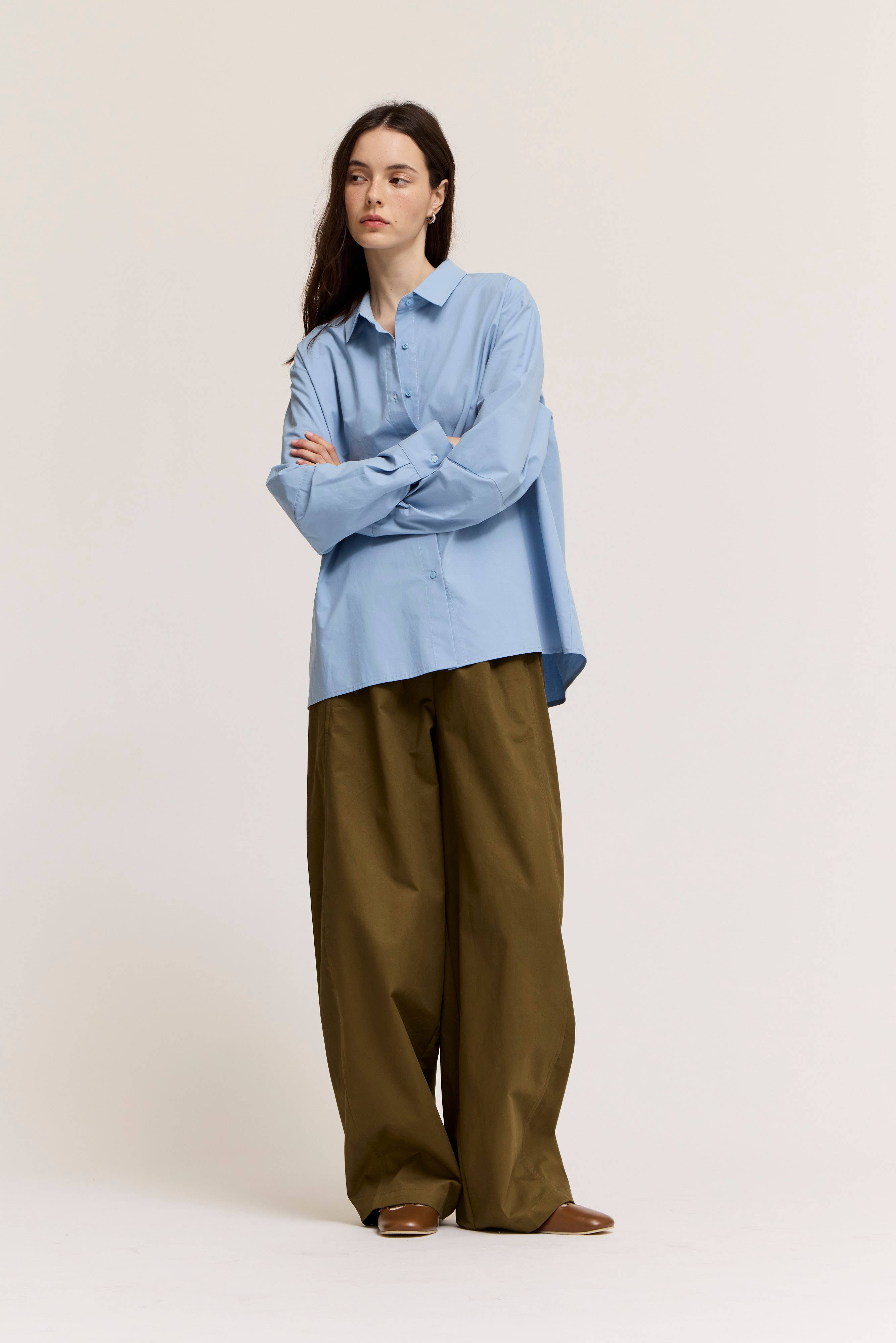Woman wearing a light blue shirt and olive green pants on a white background