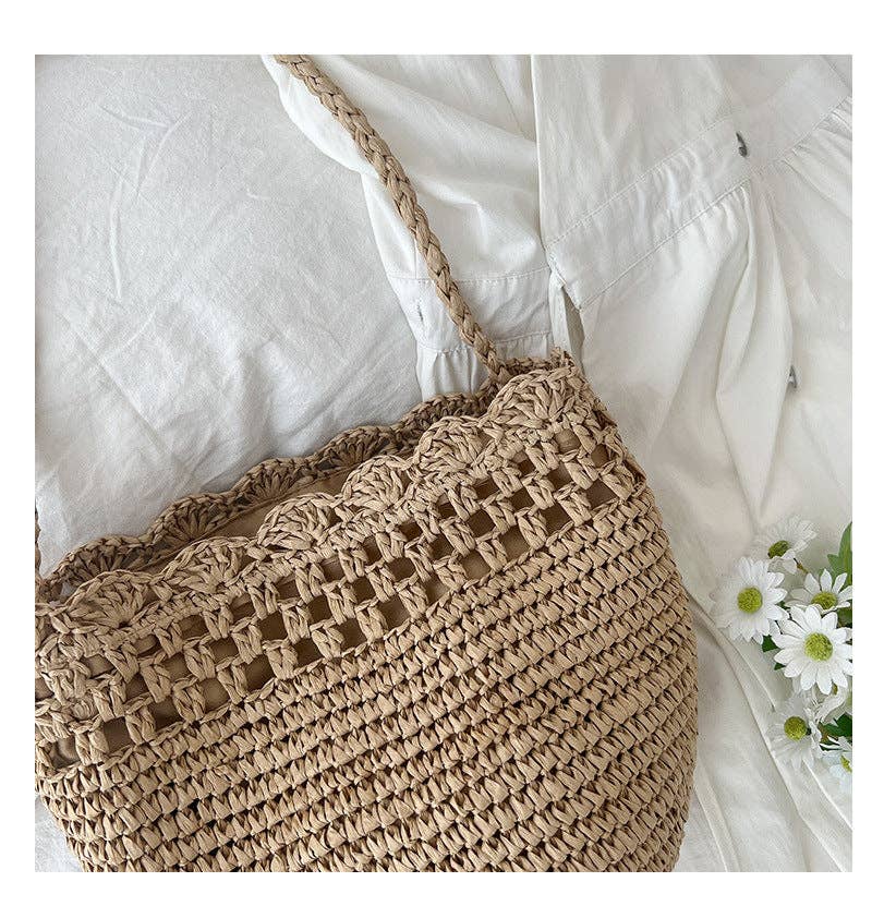 Woven beige bag on a white fabric background with a small flower arrangement.